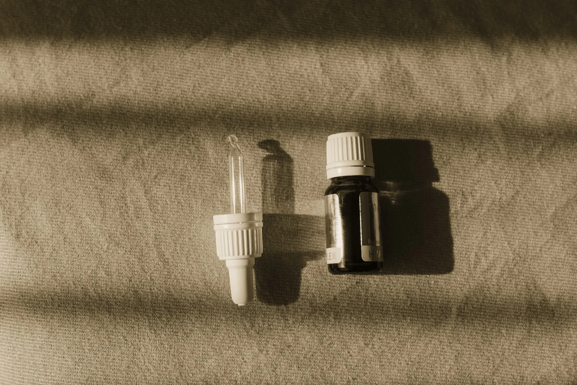 Serumflaska med pipett på beige linne i randigt solljus